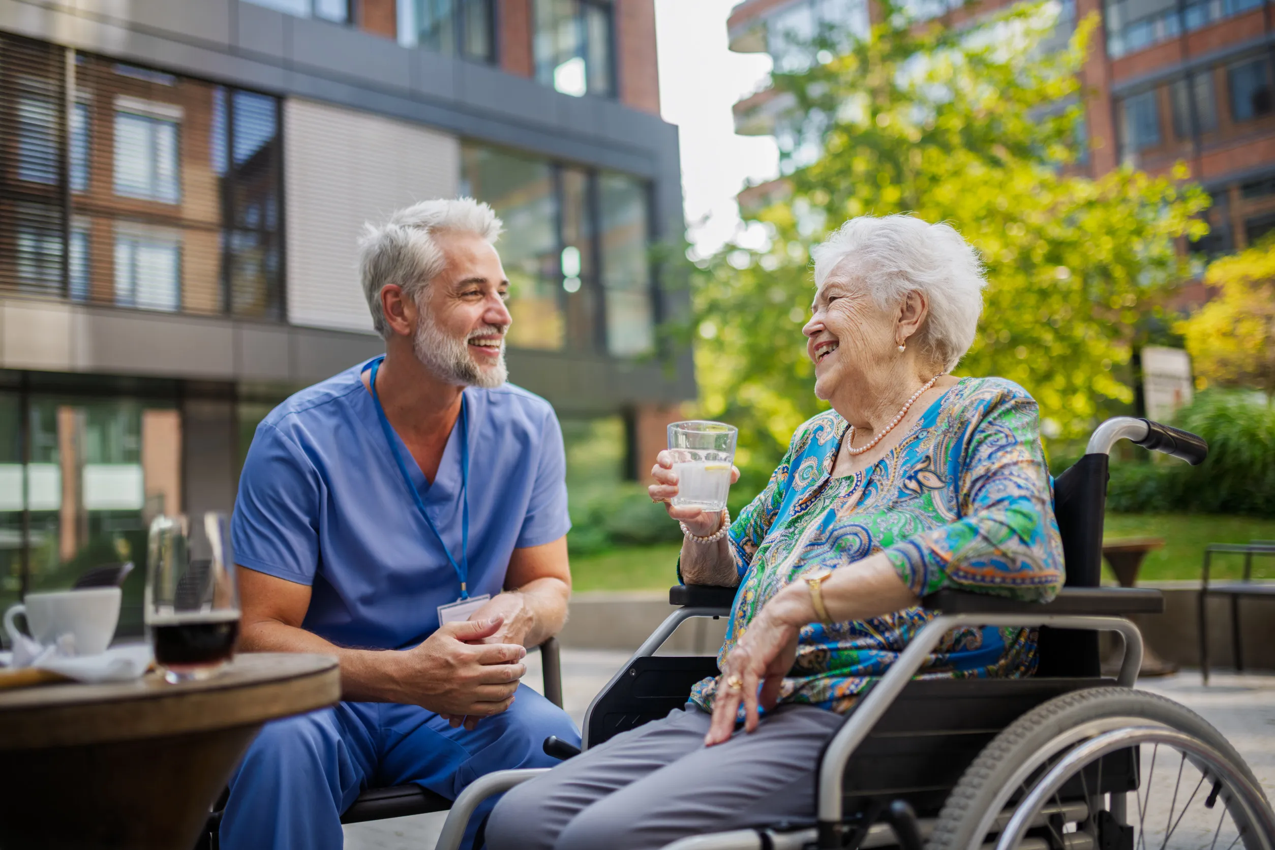 Male nurse having cup of coffee with senior patient in a wheelchair
