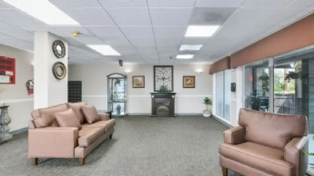 A living area with a brown couch and armchair, a small black fireplace, and decorative elements on the wall